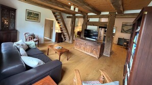 A spacious living room with a wooden ceiling, a black leather sofa, a wooden coffee table, and a television.