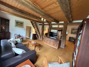 Amplia sala de estar con techo de madera, un sofá de cuero negro, una mesa de centro de madera y un televisor.