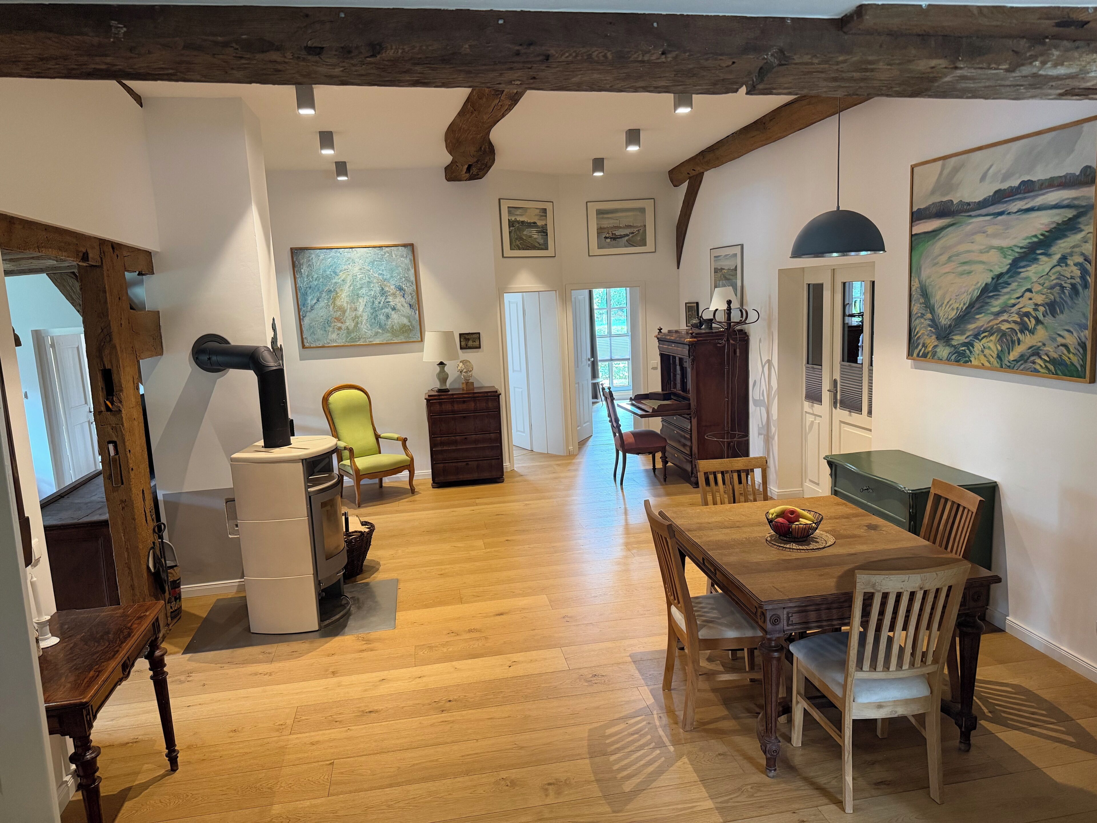 Une pièce spacieuse avec un plancher en bois, une table à manger avec des chaises, un piano et des œuvres d’art accrochées aux murs.