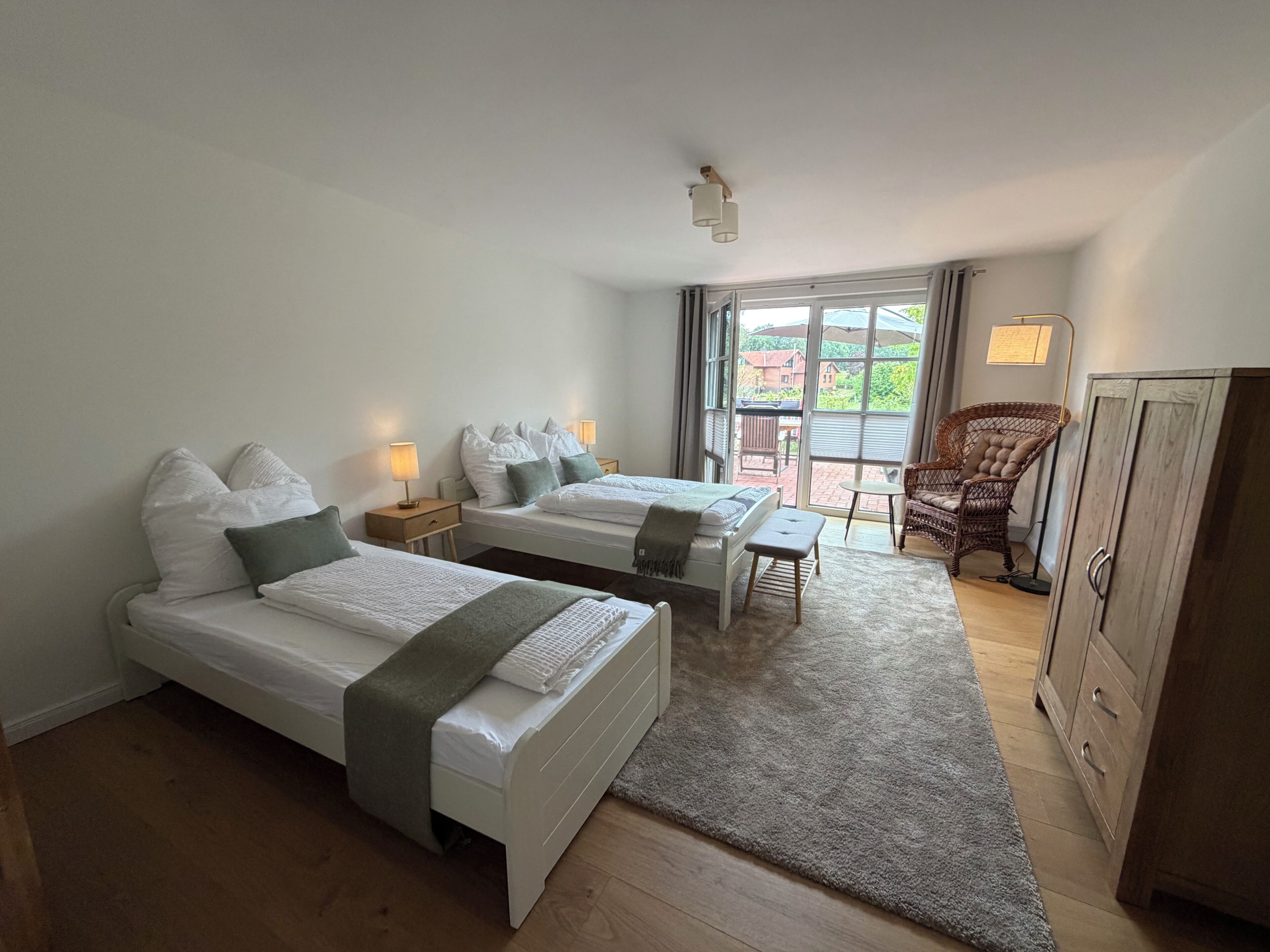 Ein Hotelzimmer mit zwei Betten, einem kleinen Tisch, einem Korbstuhl und einem Kleiderschrank.