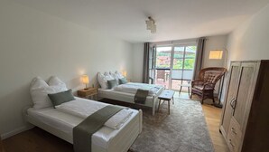Ein Hotelzimmer mit zwei Betten, einem kleinen Tisch, einem Korbstuhl und einem Kleiderschrank.