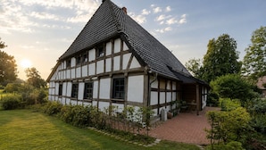 Ein traditionelles Fachwerkhäuschen mit einem steilen Satteldach, umgeben von einem gepflegten Garten und einem gepflasterten Weg.