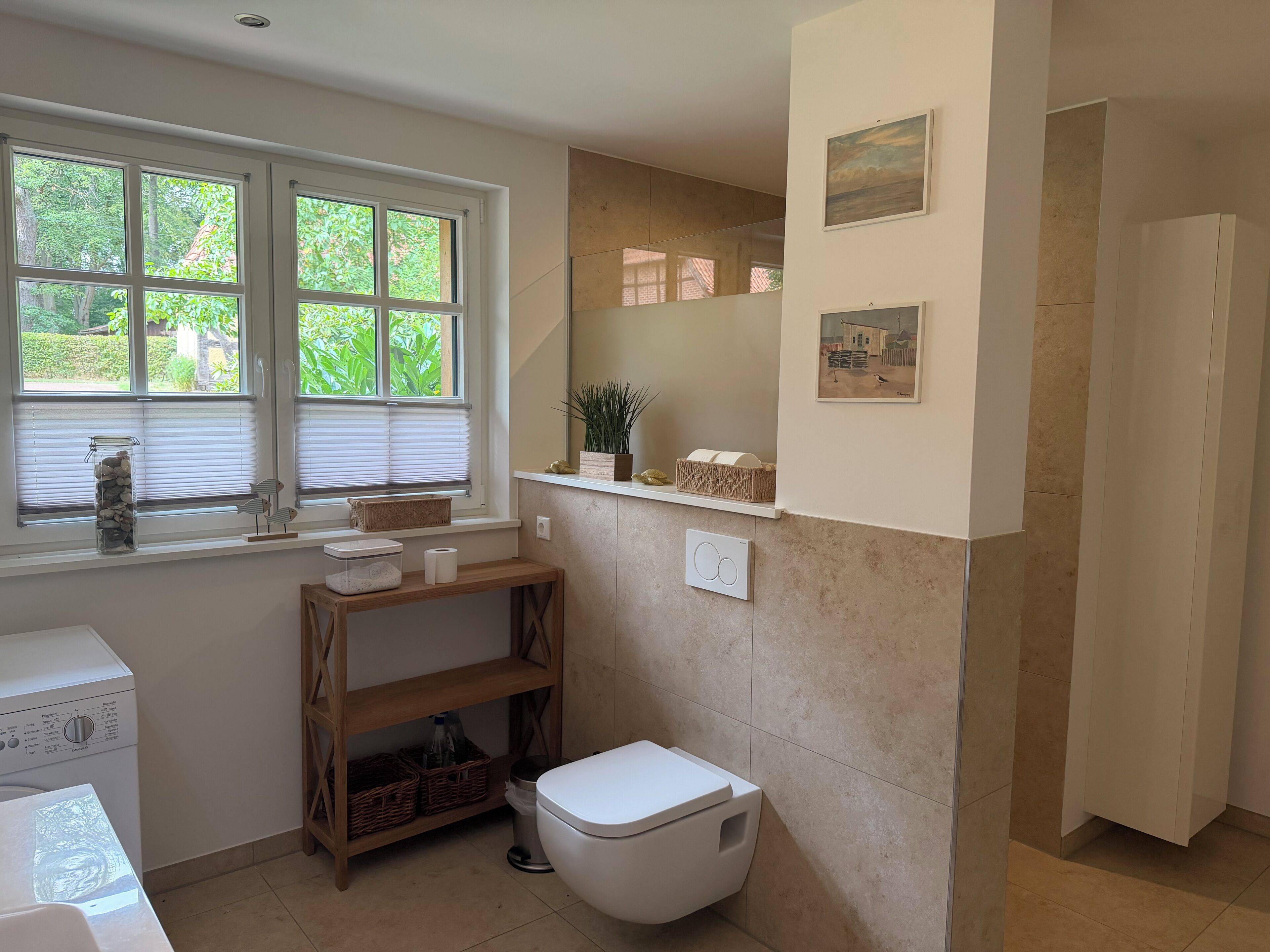 Een badkamer met toilet, wastafel, raam met zonwering en een plank met toiletartikelen.