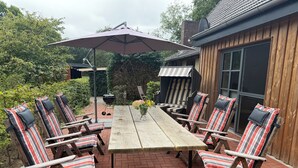 A patio with a wooden table and striped chairs, a grill, and an umbrella.