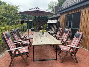 Un patio con mesa de madera, sillas a rayas, una parrilla y una sombrilla.