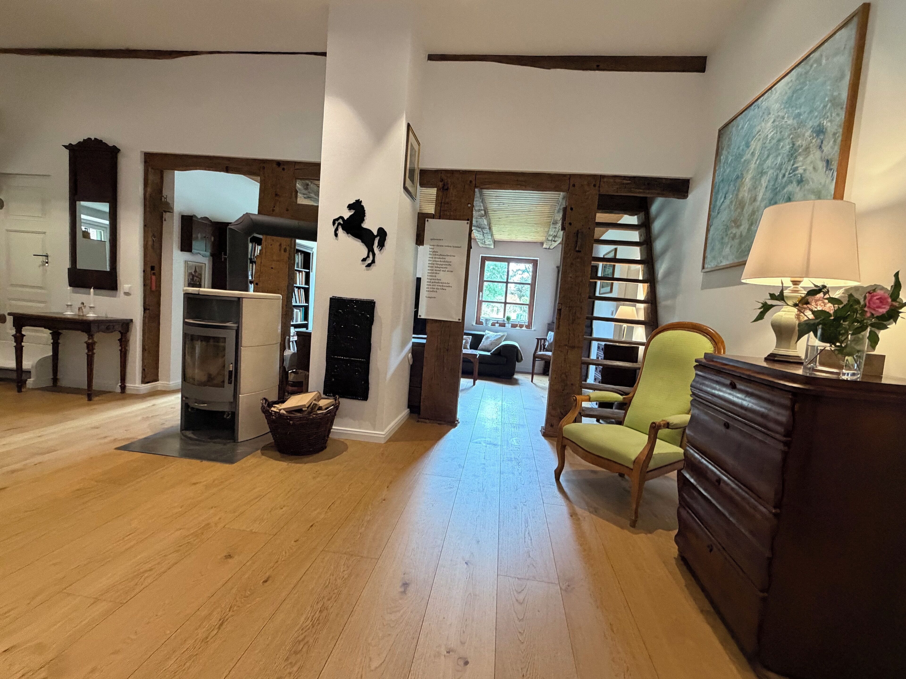 A spacious living area with a fireplace, a bookshelf, a green armchair, and a large painting on the wall.