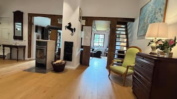 A spacious living area with a fireplace, a bookshelf, a green armchair, and a large painting on the wall.