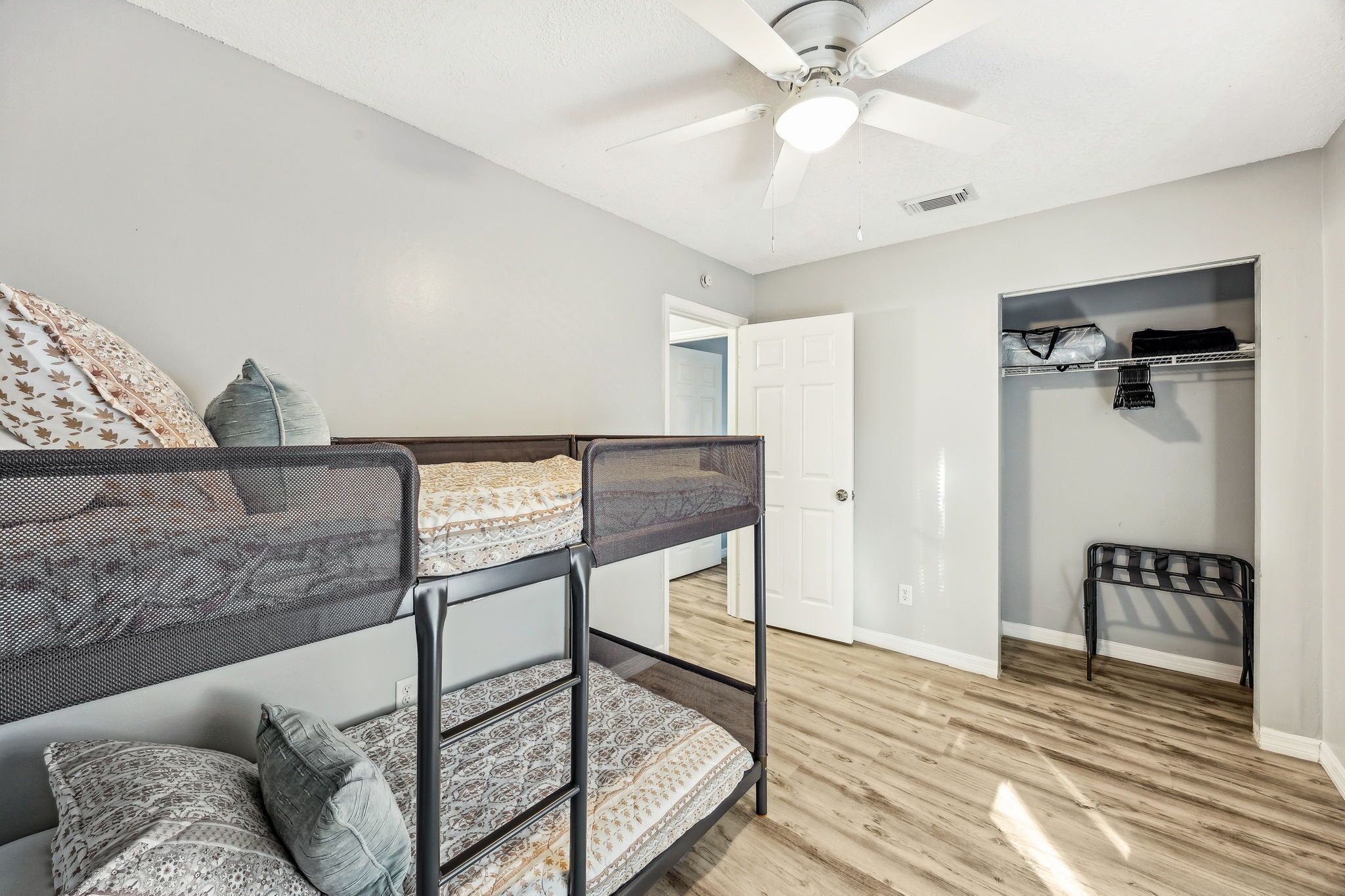 A bunk bed with patterned bedding, a ceiling fan, and a wooden floor.