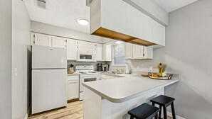 A modern kitchen with white cabinetry, a central island, and black bar stools. - Amelia Island 3 Bedroom Sea Escape (Fernandina Beach)