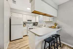 A modern kitchen with white cabinetry, a central island, and black bar stools. - Amelia Island 3 Bedroom Sea Escape (Fernandina Beach)