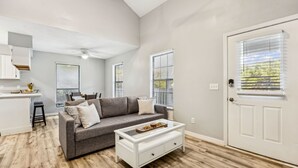 A modern living room with a gray sofa, a white coffee table, and a dining area with a white countertop and bar stools. - Amelia Island 3 Bedroom Sea Escape (Fernandina Beach)