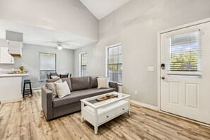 A modern living room with a gray sofa, a white coffee table, and a dining area with a white countertop and bar stools. - Amelia Island 3 Bedroom Sea Escape (Fernandina Beach)