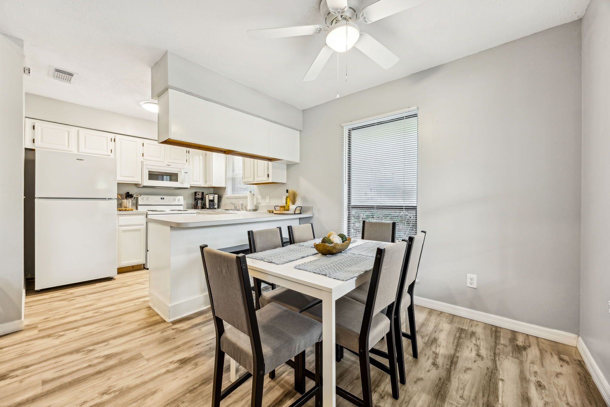A modern kitchen with white cabinets, a central island, and a dining area with a white table and chairs.