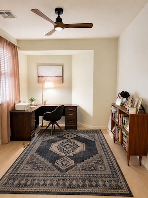 Ein Home-Office mit Schreibtisch, Stuhl, Bücherregal und einem großen Teppich.