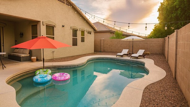 A swimming pool with a curved edge, surrounded by a brick wall and a covered patio area with lounge chairs and umbrellas. - Charming 3-bedroom Luxury Home, Perfect for Entertaining (Waddell)