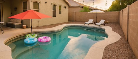 A swimming pool with a curved edge, surrounded by a brick wall and a covered patio area with lounge chairs and umbrellas.