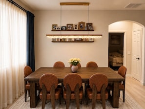 A dining area with a wooden table and six chairs, a vase of flowers, and a wall-mounted light fixture. - Charming 3-bedroom Luxury Home, Perfect for Entertaining (Waddell)