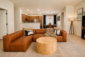 A modern living room with a sectional sofa, a round coffee table, and a kitchen in the background. - Charming 3-bedroom Luxury Home, Perfect for Entertaining (Waddell)