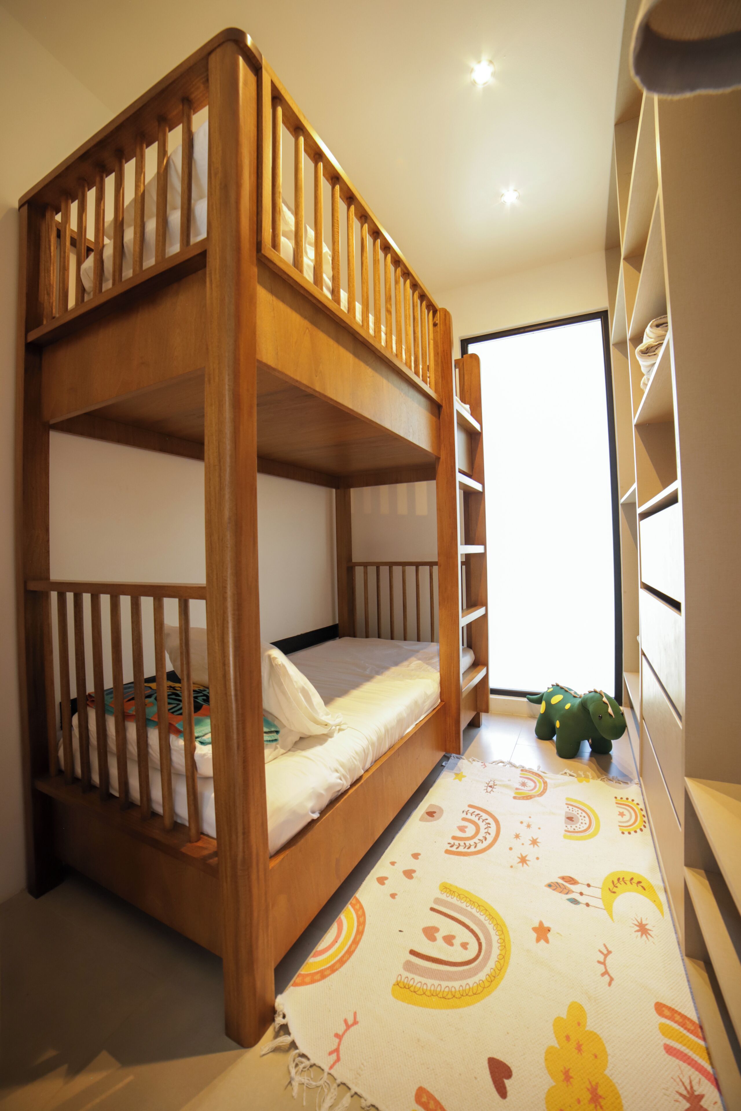 Una cama litera con estructura de madera, colchón blanco y un tapete de colores en el suelo.
