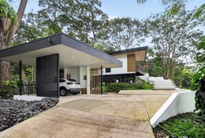 Una casa moderna con un camino de entrada cubierto, una escalera y un automóvil estacionado afuera.