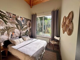 A bedroom with a large bed, a window with curtains, a chair, and a wall with a tropical mural.