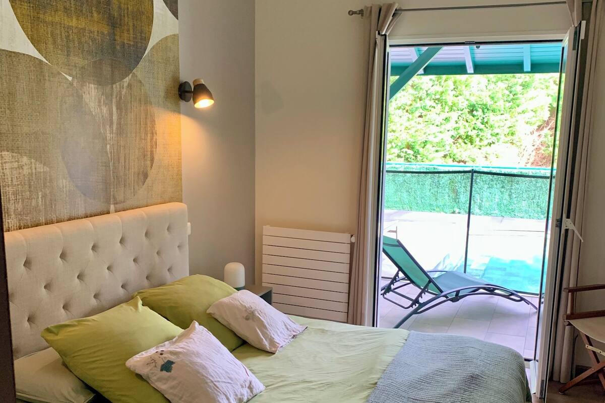 A bedroom with a large bed, a headboard, a wall-mounted light, and a view of an outdoor balcony.