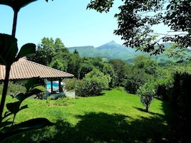 A house with a tiled roof, surrounded by lush greenery and a mountain in the background.