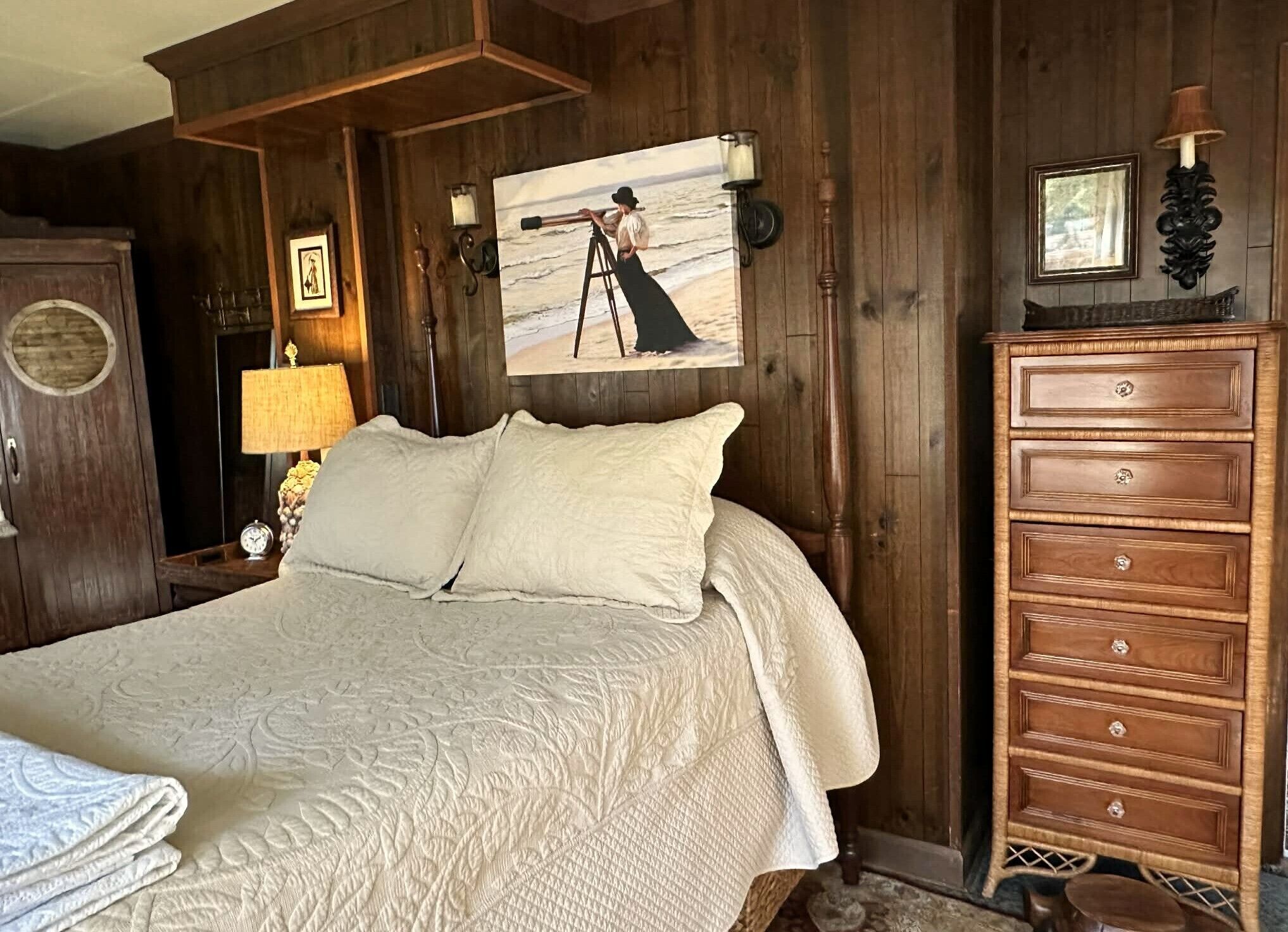 Une chambre à coucher avec un grand lit, des murs en bois, une commode et un tableau représentant une femme sur une échelle.