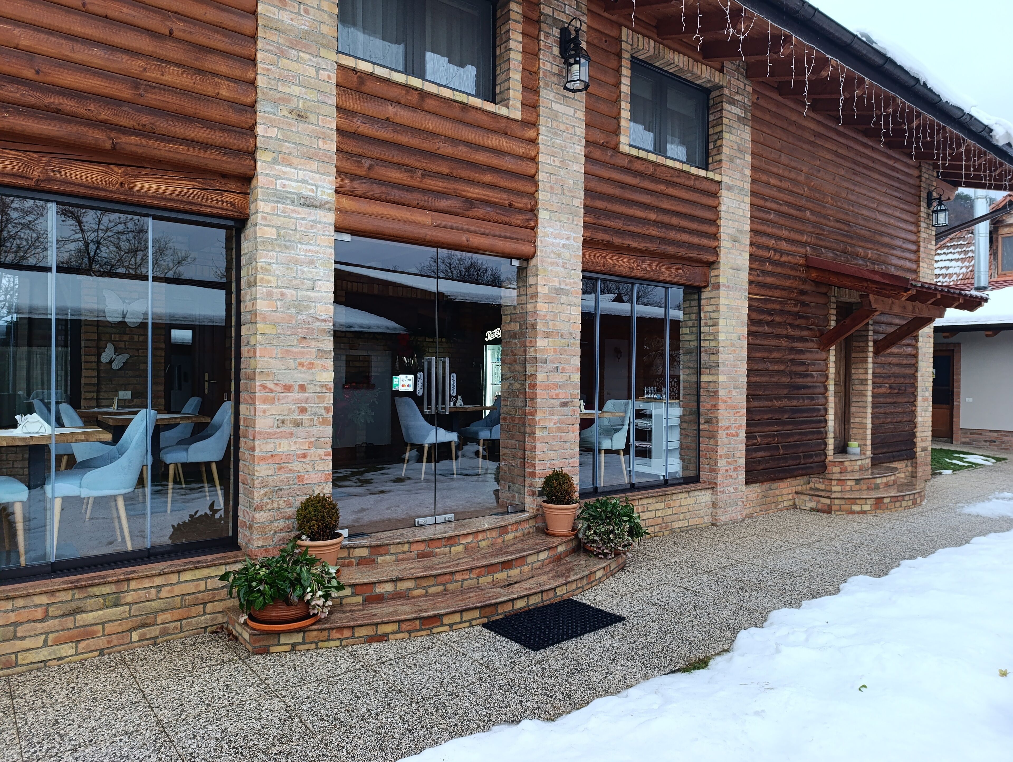 A log cabin-style building with large windows, outdoor seating, and potted plants.