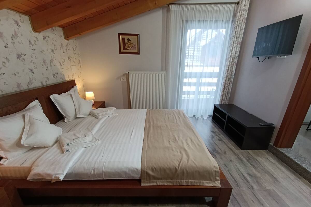 A neatly made bed with white linens, a wooden headboard, a bedside lamp, and a wall-mounted TV.