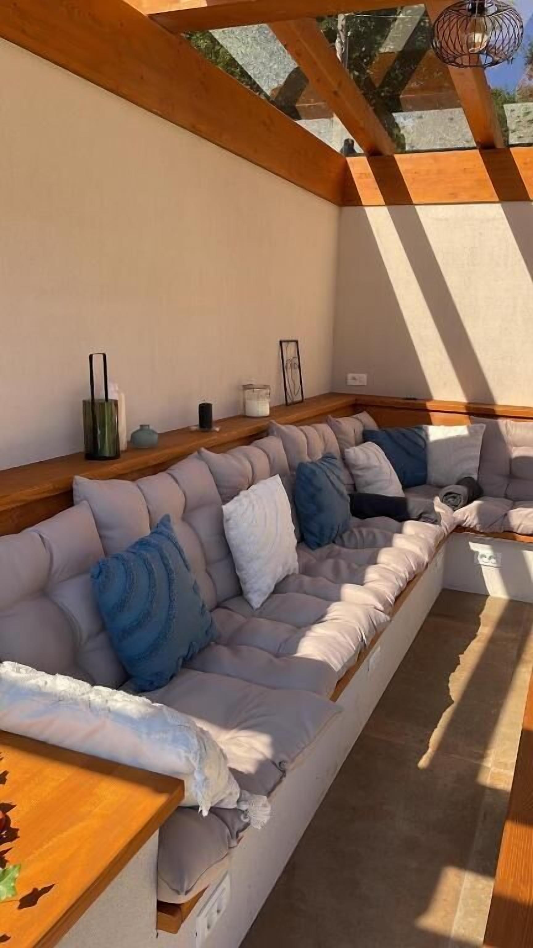 A modern living room with a large L-shaped sectional sofa, wooden beams on the ceiling, and a view of the outdoors.