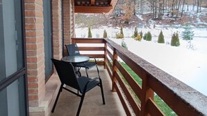 A covered patio with a brick wall, a wooden railing, and a view of a snowy landscape. - Villa Diva (Budureasa)
