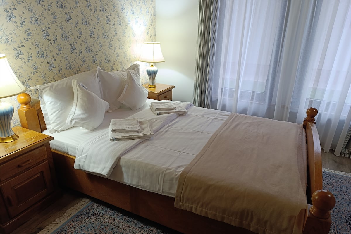 A neatly made bed with white linens, a wooden headboard, and a bedside table with a lamp.