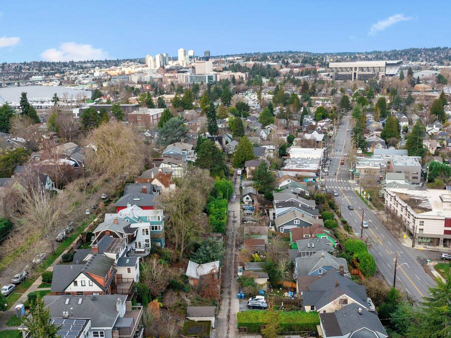 A residential area with houses, streets, and a distant view of a city skyline including a bridge and a stadium.