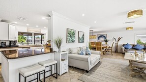Eine moderne Küche mit Kochinsel, ein Essbereich mit Tisch und Stühlen sowie ein Wohnbereich mit Sofa und Couchtisch.