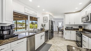 A modern kitchen with white cabinetry, stainless steel appliances, and a view of a pool. - Indulge in your Marco Island Haven. (Marco Island)