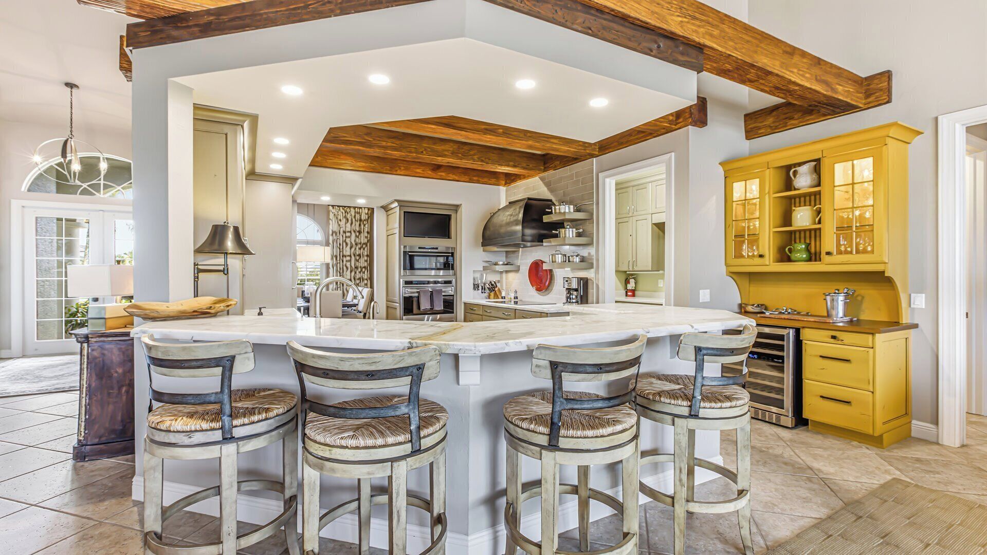 A kitchen with a large island, bar stools, and yellow cabinets.