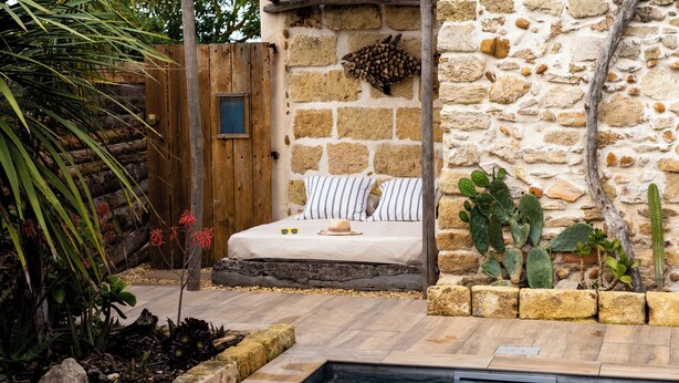 Une pièce aux murs de pierre, avec un lit, une petite porte en bois et un espace piscine.