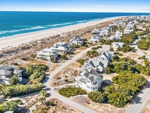 Eine Wohngegend an der Küste mit Häusern entlang des Strandes, die eine Mischung aus ein- und mehrgeschossigen Gebäuden zeigt, von denen einige große Fenster und Balkone haben, mit freiem Blick auf den Ozean.