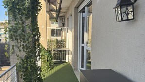 En balkon med græs, et sort skab og et hvidt metalhegn.
