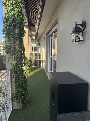 Ein Balkon mit Kunstgrasanlage, einem schwarzen Schrank und einem weißen Metallzaun.