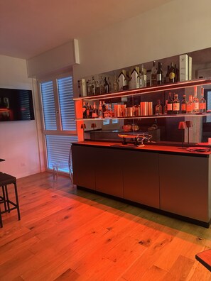 Eine moderne Küche mit einer zentralen Kochinsel, Holzböden und einer Bar, die mit verschiedenen Flaschen und Gläsern bestückt ist.