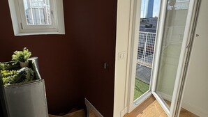 Et værelse med brun væg, et vindue, en skydedør af glas og en lille balkon med udsigt til bygninger.