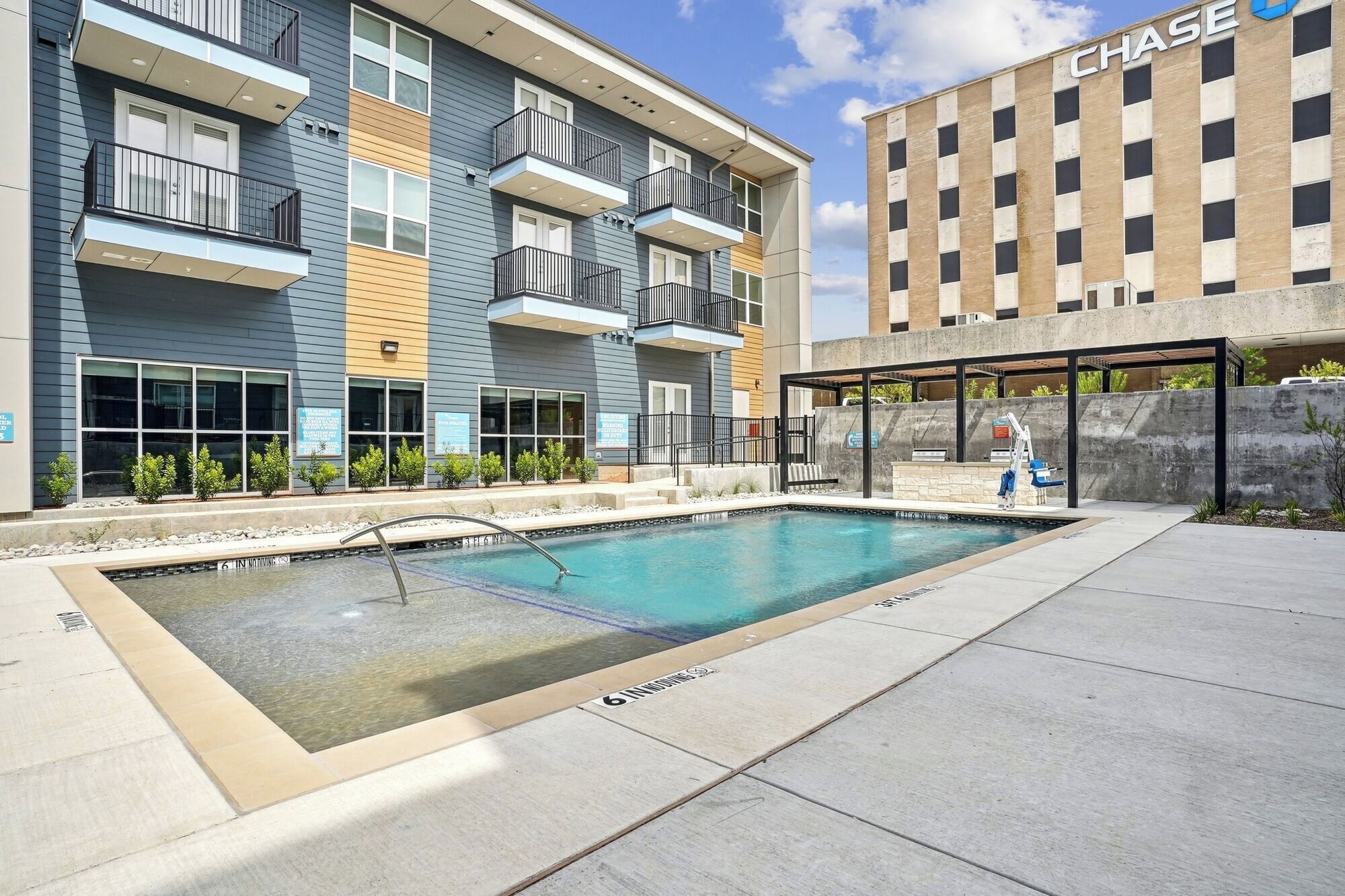 A modern apartment building with a pool area, including a lounge and a covered seating area.