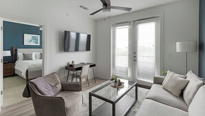 A modern living room with a sofa, a glass coffee table, a desk, and a bed. - Landing Apartments Garland, TX (Garland)