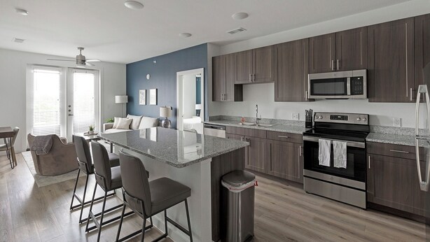 A modern kitchen with dark wood cabinets, a stainless steel refrigerator, a microwave, and a black stove. - Landing Apartments Garland, TX (Garland)