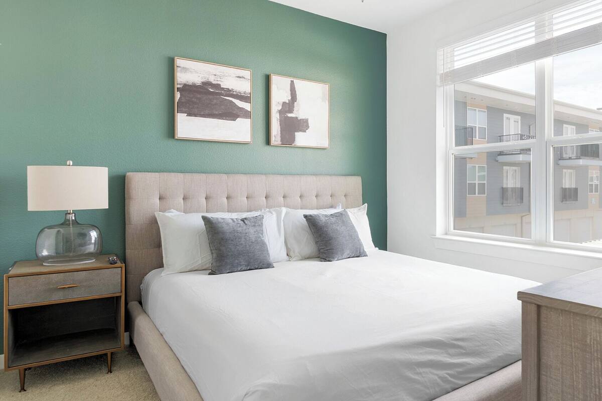 A bedroom with a large bed, a nightstand, a lamp, and two framed pictures on the wall.