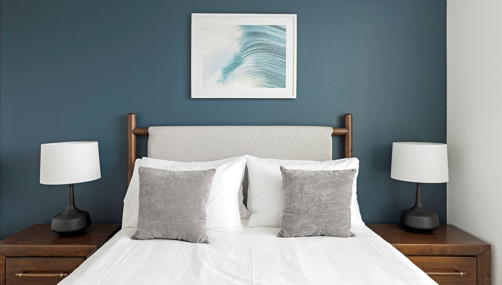 A neatly made bed with white and gray pillows, two bedside lamps, and a framed artwork above the headboard.