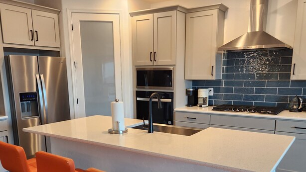 A modern kitchen with a central island, stainless steel appliances, and orange bar stools. - Casa Limpia Tucson! (Tucson)