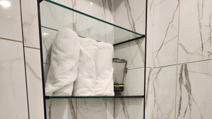 A bathroom with marble walls and a glass shelf holding towels. - Casa Limpia Tucson! (Tucson)